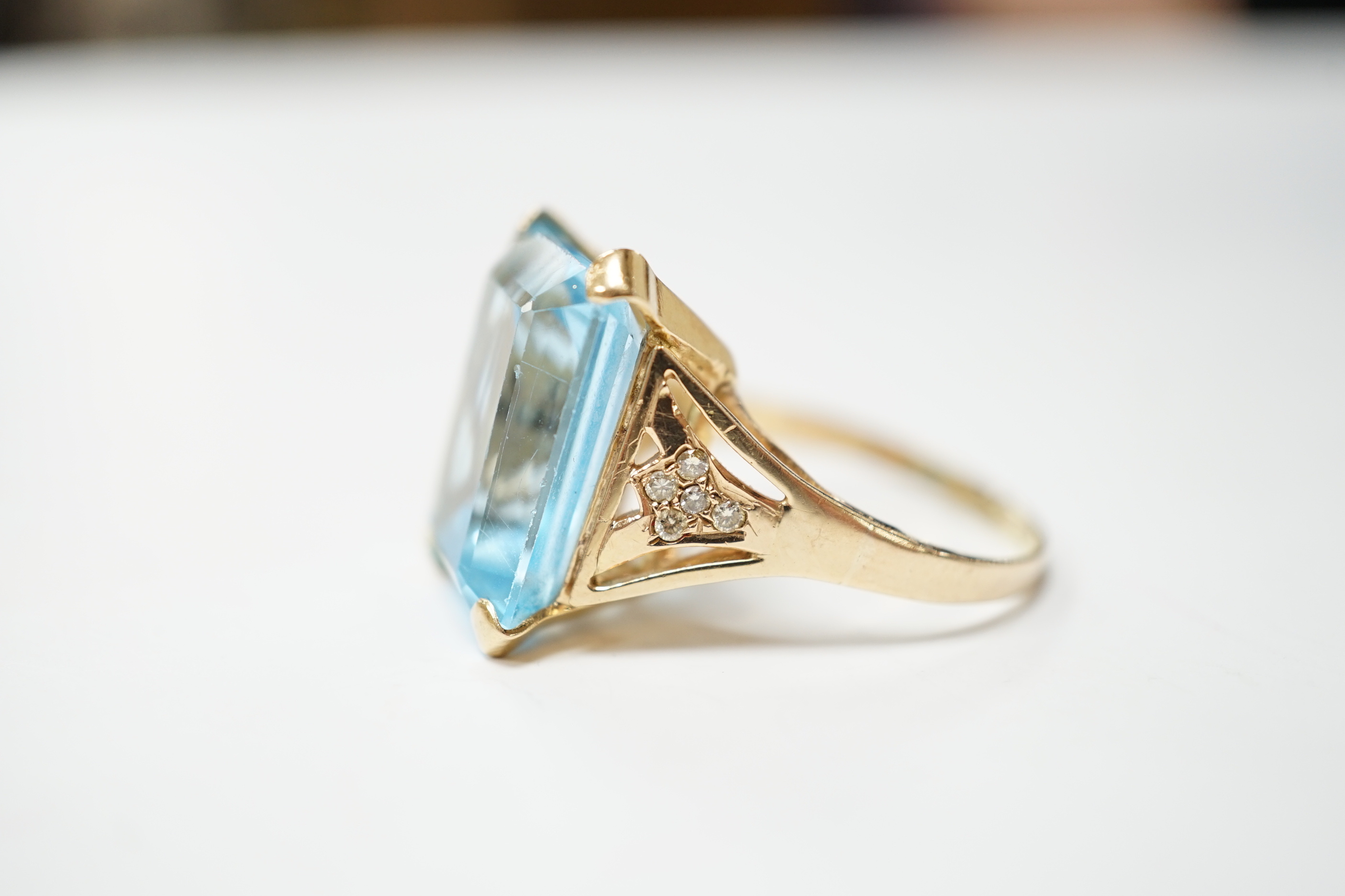 A yellow metal and single stone emerald cut blue topaz set dress ring, with ten stone diamond chip set shoulders, size U/V, gross weight 10.4 grams.